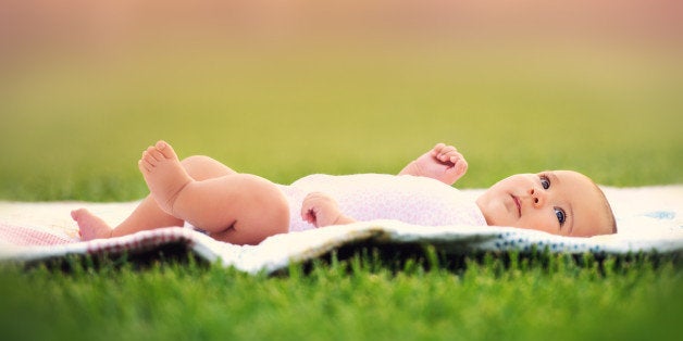 A sweet baby girl laying on a quilt in the grass.