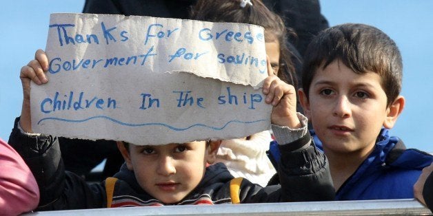 Migrant children display on November 27, 2014 a sign upon their arrival in the Cretan port of Ierapetra. Around 700 migrants aboard a freighter that had been drifting in the Aegean Sea for two days began disembarking on the Greek island of Crete. The migrants from Syria, Afghanistan, Iran and Iraq, include 'a lot of women and children', said Theodosis Kalantzakis, the mayor of Ierapetra. AFP PHOTO / COSTAS METAXAKIS (Photo credit should read Costas Metaxakis/AFP/Getty Images)