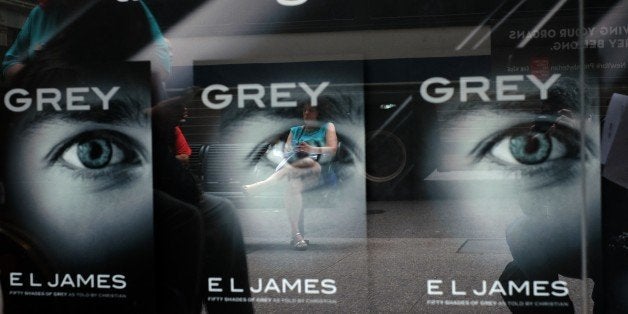 A woman sitting on a bench is reflected on a glass window advertising E.L James's new book 'Grey: Fifty Shades of Grey as Tol