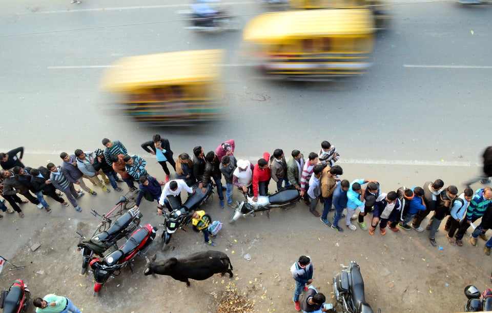 People stand in a queue outside of an ATM as they wait to withdraw money in Allahabad on December 13,