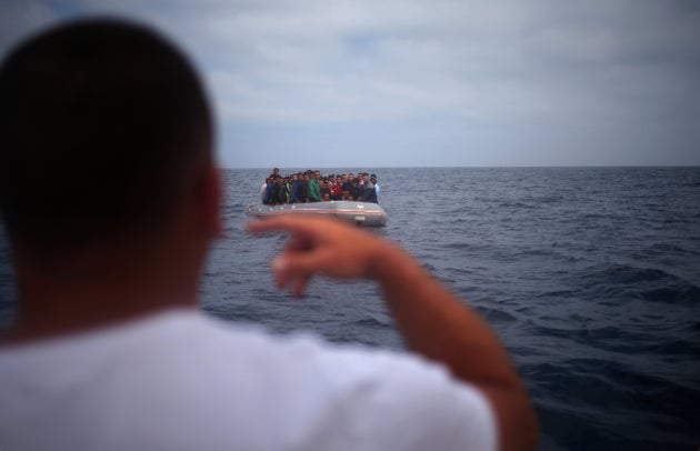 Un pêcheur s'entretient avec des migrants depuis un bateau avant de descendre d'un dériveur sur la plage