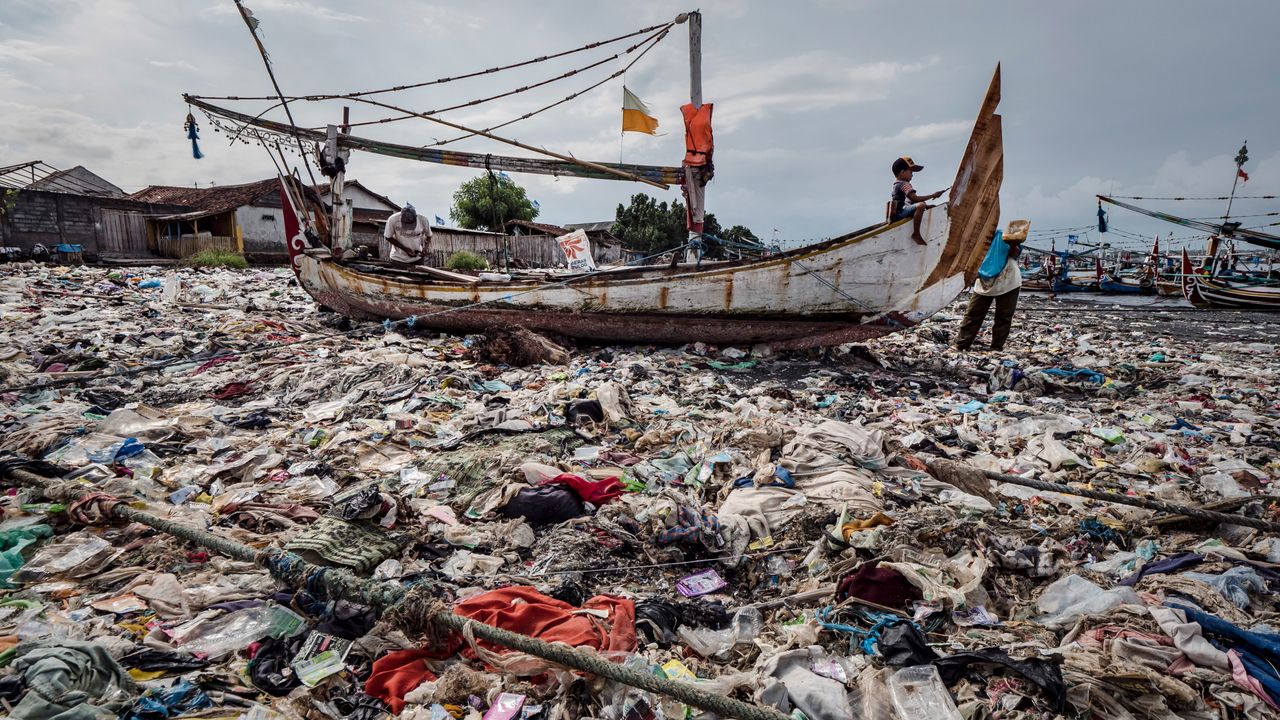 A boy paints a boat sitting on a beach smothered in plastic waste at Muncar port in Banyuwangi, East Java, Indonesia, on March 4, 2019.