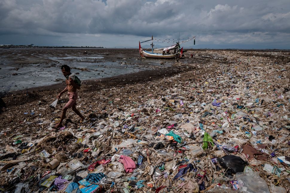 A man walks on a beach filled with plastic waste at Muncar