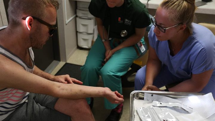 Two University of Miami medical students examine the track marks of a patient at the IDEA Exchange, which offers free wound care and HIV screenings. Southern states are embracing harm reduction techniques, including naloxone and needle exchanges, more than ever before. But some conservatives say there’s a limit to their support.