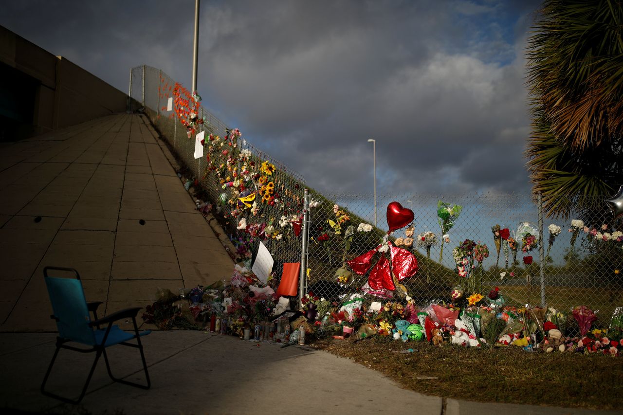 An empty chair is seen in front of flowers and mementoes placed on a fence to commemorate the victims of the mass shooting at Marjory Stoneman Douglas High School.