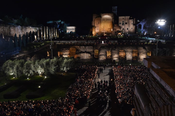 Christians carry a cross toward Pope Francis, visible in the background, during a torchlight procession on Good Friday in Rome.