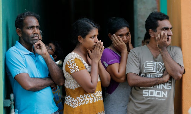 Sri Lankans living nearby watch as security forces officers inspect a suspicious vehicle parked near...