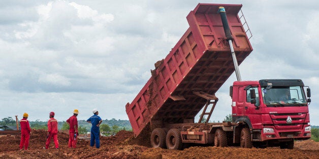Workers watch as a truck unloads land at a ShanDong ZhongJiao Navigation Engineering Co. construction site as a new port is built near Boke, Guinea, on Tuesday, Sept. 8, 2015. Building the port only took about eight months and allowed China Hongqiao Group Ltd.s project to start shipping in July. Photographer: Waldo Swiegers/Bloomberg via Getty Images