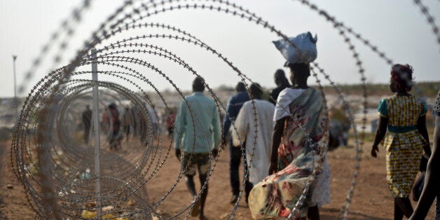 FILE- In this file photo taken Tuesday, Jan. 19, 2016,displaced people walk next to a razor wire fence at the United Nations base in the capital Juba, South Sudan. A U.N. report describing sweeping crimes like children and the disabled being burned alive and fighters being allowed to rape women as payment shows South Sudan is facing "one of the most horrendous human rights situations in the world," the U.N. human rights chief said Friday, March 11, 2016. (AP Photo/Jason Patinkin, File)