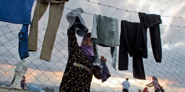 A woman hangs her clothes to dry on a barbed wire fence at the migrants camp in Idomeni, Greece, Thursday, May 19, 2016. Tho