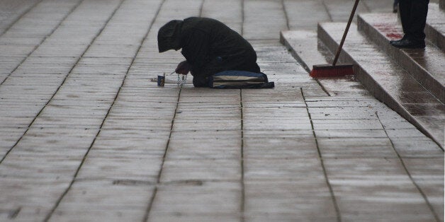 A beggar kneels on the ground as a man sweeps away rubbish from new year's celebrations in Stuttgart, southern Germany, on January 1, 2016. / AFP / dpa / Marijan Murat / Germany OUT (Photo credit should read MARIJAN MURAT/AFP/Getty Images)