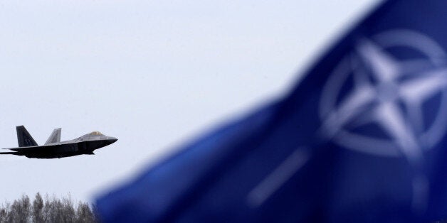 NATO flag flutters as U.S. Air Force F-22 Raptor fighter flies over the military air base in Siauliai, Lithuania, April 27, 2016. REUTERS/Ints Kalnins