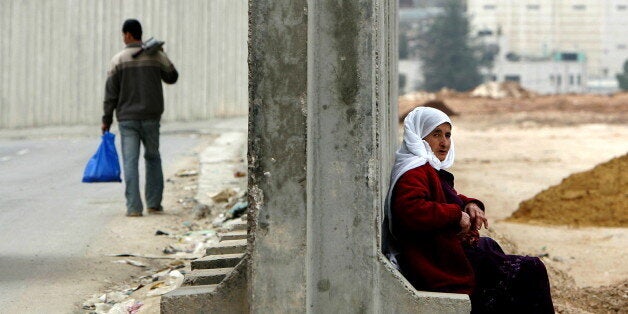 A Palestinian woman sits on part of the Israeli security barrier in the West Bank town of Ram near the checkpoint Qalandia February 20, 2005. [Israel's cabinet met on Sunday in a pivotal session expected to give the go-ahead to evacuate Jewish settlers from occupied Gaza and for the first time remove settlements from land where Palestinians want a state.]