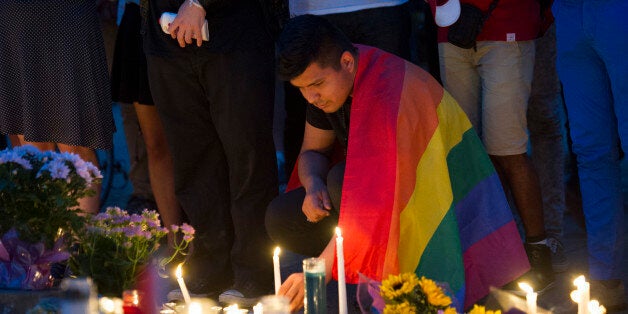 An unidentified man, wrapped in a Rainbow Flag, lights a candle during a vigil in Washington, Monday June 13, 2016, hosted by