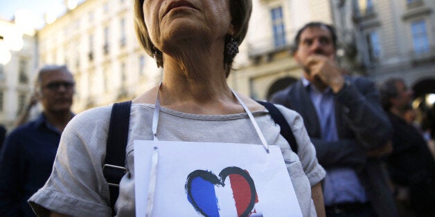 A woman wears a banner displaying the colours of France's flag in a heart during a minute of silence in front of the City Hal