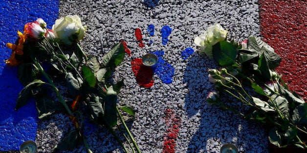 A painting with the colors of the French flag covers the asphalt near a makeshift memorial to honor the victims, three days after a truck mowed through revelers, on the famed Promenade des Anglais in Nice, southern France, Sunday, July 17, 2016. French authorities detained two more people Sunday in the investigation into the Bastille Day truck attack on the Mediterranean city of Nice that killed at least 84 people, as authorities try to determine whether the slain attacker was a committed religious extremist or just a very angry man. (AP Photo/Francois Mori)