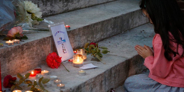 A young girl prays near flowers and candles at the town hall in Saint-Etienne-du-Rouvray, near Rouen in Normandy, France, to