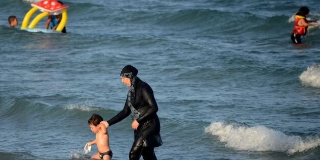 A Tunisian woman wearing a 'burkini', a full-body swimsuit designed for Muslim women, walks in the water with a child on Augu