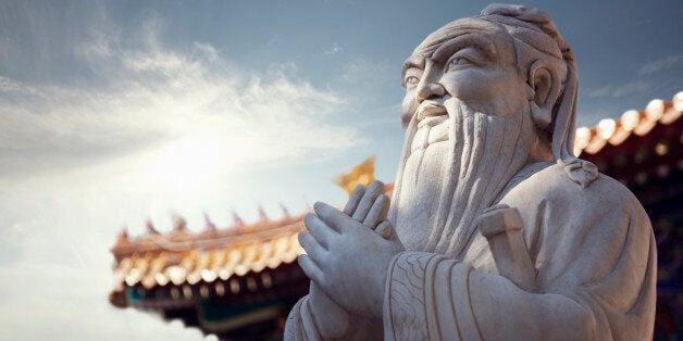 Close-up of stone statue of Confucius, pagoda roof in the background