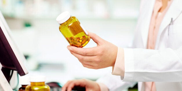 Midsection of female pharmacist holding pill bottle. Professional is using computer keyboard at desk. Chemist is in drug store. Focus is on medicine bottle held by expert.