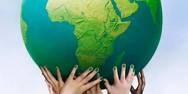Multiracial hands holding green globe against sky background 