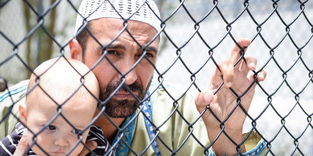 Muslim refugee holding his baby looking through a fence