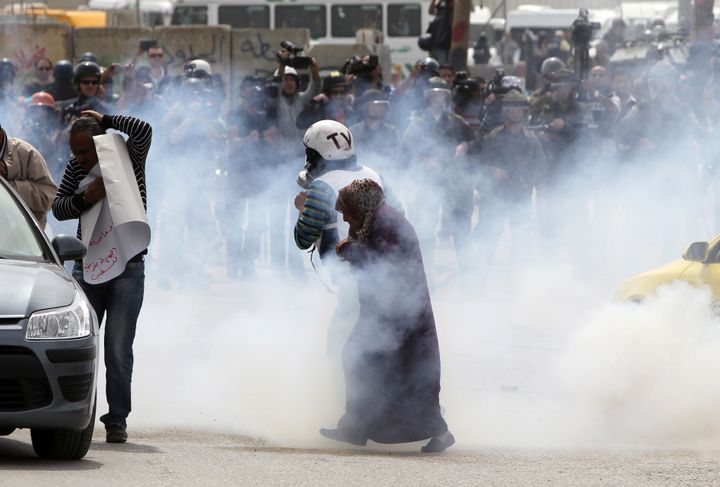 A journalist and an elderly woman walk away from tear gas smoke during clashes between Palestinians protesters and Israeli soldiers following a rally commemorating the 37th anniversary of 'Land Day', on March 30, 2013 near the Qalandia checkpoint in the Israeli occupied West Bank. Nearly 200 Palestinians clashed with Israeli forces in Qalandia, who responded with tear gas. AFP PHOTO/ ABBAS MOMANI (Photo credit should read ABBAS MOMANI/AFP/Getty Images)