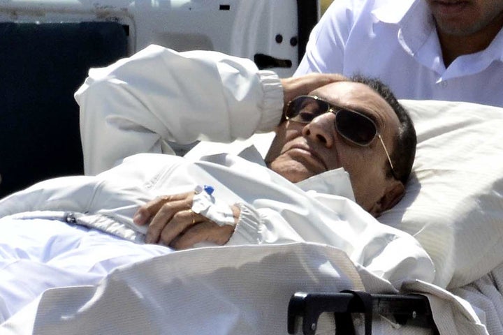 Ousted Egyptian president Hosni Mubarak (C) is wheeled out of an ambulance outside the Maadi military hospital following a hearing in Cairo on April 13, 2013. The judge in the retrial of Mubarak recused himself, in a chaotic opening hearing that lasted just seconds and saw a proud and combative Mubarak smile and wave in the dock. AFP PHOTO/ MOHAMED EL-SHAHED (Photo credit should read MOHAMED EL-SHAHED/AFP/Getty Images)