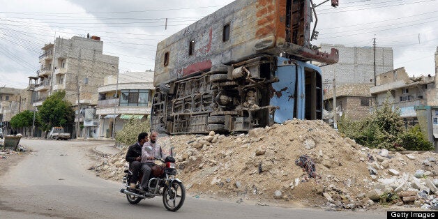 Syrian civilians ride past two destroyed buses piled up on rubble in the northern city of Aleppo on April 22, 2013. The Euro