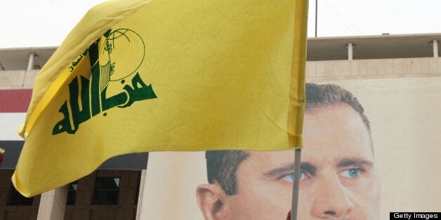 Syrian demonstrators hold up a Lebanese Hezbollah flag in front of a portrait of President Assad, during a rally to show their support for their leader and the Syrian army in central Damascus on February 14, 2012. AFP PHOTO/LOUAI BESHARA (Photo credit should read LOUAI BESHARA/AFP/GettyImages)