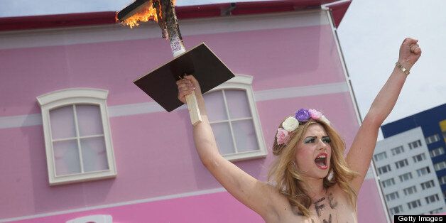 BERLIN, GERMANY - MAY 16: A bare-breasted FEMEN protester with an inscription on her body that reads: 'Life In Plastic Is Not Fantastic' yells protest slogans while holding up a burning cross with a Barbie doll attached to it outside the Barbie Dreamhouse Experience on May 16, 2013 in Berlin, Germany. The Barbie Dreamhouse is a life-sized house full of Barbie fashion, furniture and accessories and will be open to the public until August 25 before it moves on to other cities in Europe. (Photo by Sean Gallup/Getty Images)