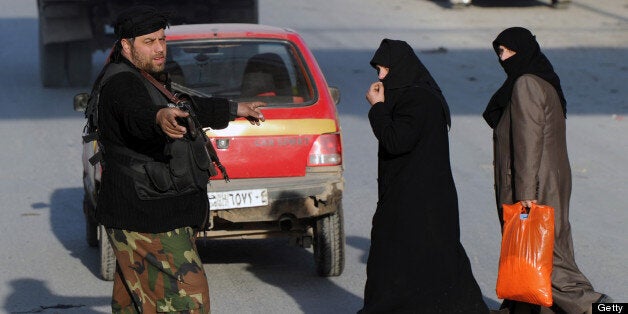 A Syrian rebel fighter helps women cross the road at a check point in Aleppo's old city on January 16, 2013. Syria's transpor
