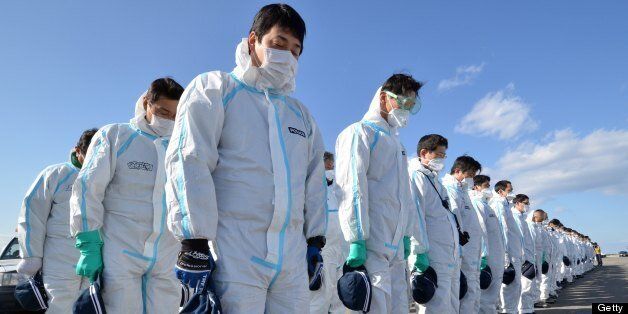 Police officers in radiation protection suits bow their heads to offer prayers in silence for tsunami victims in Namie, near the striken TEPCO's Fukushima Dai-ichi nuclear plant in Fukushima prefecture on March 11, 2013. March 11, 2013 marks the second anniversary of the 9.0 magnitude earthquake that sent a huge wall of water into the coast of the Tohoku region, splintering whole communities, ruining swathes of prime farmland and killing nearly 19,000 people. AFP PHOTO / YOSHIKAZU TSUNO (Photo credit should read YOSHIKAZU TSUNO/AFP/Getty Images)