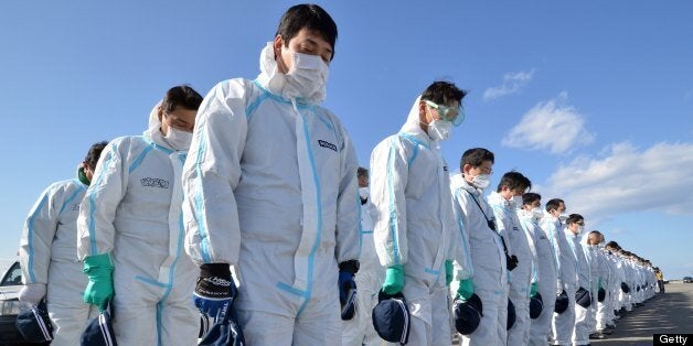 Police officers in radiation protection suits bow their heads to offer prayers in silence for tsunami victims in Namie, near