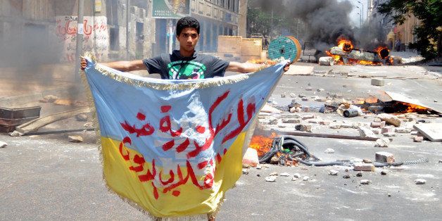A supporter of the Muslim Brotherhood and Egypt's ousted president Mohamed Morsi holds a banner reading in Arabic: 'Alexandria is against the coup' as protestors set fire to a council building in Egypt's northern coastal city of Alexandria on August 14, 2013. Clashes broke out following a demonstration against security forces clearing two pro-Morsi protest camps in Cairo. AFP PHOTO / STR (Photo credit should read STR/AFP/Getty Images)
