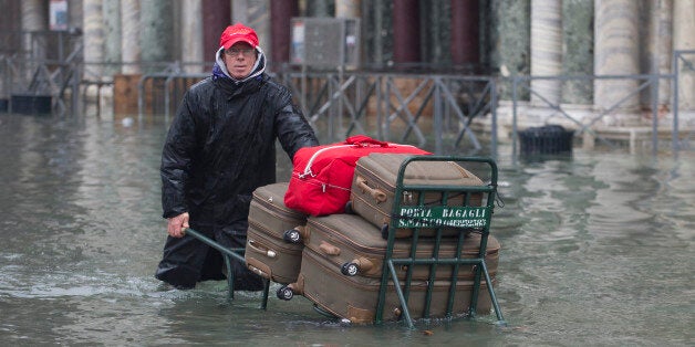 VENICE, ITALY - NOVEMBER 19: A baggage porter struggles under torrential rain and wind during High Water on November 19, 2013 in Venice, Italy. Venice will be affected by the high water for the next few days due to the passage of Cyclone Cleopatra that hit the Italian island of Sardinia causing devastating flooding, which has left at least 17 dead. (Photo by Marco Secchi/Getty Images)