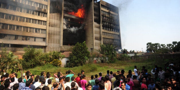 Bangladeshi bystanders watch as smoke and flames billow from a burning garment factory in the key garment manufacturing hub of Gazipur on the outskirts of Dhaka on November 29, 2013. Bangladesh police said that they were investigating a suspected arson attack on one of the country's largest garment factories which produces clothes for Western brands. AFP PHOTO/Munir uz ZAMAN (Photo credit should read MUNIR UZ ZAMAN/AFP/Getty Images)