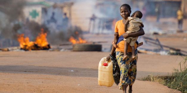 A woman carrying her child walks past the Cocoro market in the PK5 district of Bangui on January 2, 2014 after members of the Muslim community burned wood and tyres to block a road to protest against the presence of French troops of the Sangaris Operation in their neighborhood. Around 4,000 African peacekeepers and 1,600 French troops are attempting to curb escalating religious strife in the country where weeks of violence have pitted majority Christians against Muslims, who make up about one-fifth of the population. AFP PHOTO / MIGUEL MEDINA (Photo credit should read MIGUEL MEDINA/AFP/Getty Images)