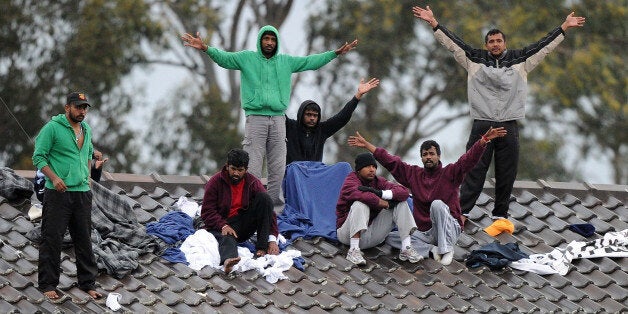 Sri Lankan asylum-seekers wave to supporters as they threaten to jump off the roof of the Villawood detention centre during an immigration protest near Sydney on September 21, 2010. The protest follows the death of Fiji's Josefa Rauluni, age 36, who lept from a roof at Villawood after receiving deportation orders on September 20. AFP PHOTO / Torsten BLACKWOOD (Photo credit should read TORSTEN BLACKWOOD/AFP/Getty Images)