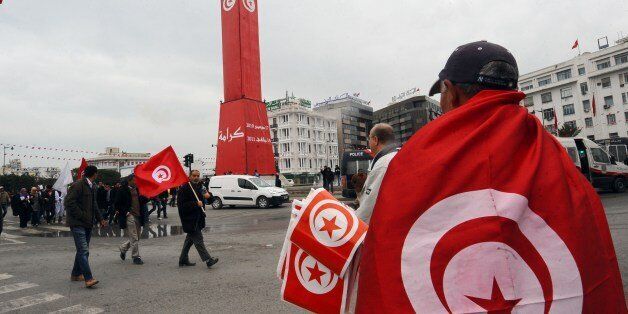 A man distributes flags next to a clock tower as Tunisians attend a rally marking the third anniversary of the uprising that ousted long-time dictator Zine El Abidine Ben Ali on January 14, 2014 in Habib Bourguiba Avenue in Tunis. Tunisia celebrated the third anniversary of the overthrow of a decades-old dictatorship in the first Arab Spring uprising, but political divisions have hampered the adoption of a new constitution by this symbolic deadline. AFP PHOTO / FETHI BELAID (Photo credit should read FETHI BELAID/AFP/Getty Images)