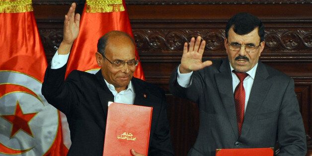 Tunisian president Moncef Marzouki (L) and outgoing Islamist prime minister Ali Larayedh wave holding copies of the new constitution after its adoption on January 27, 2014 during a ceremony at the the Tunisian National Constituent Assembly in Tunis. Tunisia's leaders signed the new constitution, a landmark event in the birthplace of the Arab Spring. AFP PHOTO / FETHI BELAID (Photo credit should read FETHI BELAID/AFP/Getty Images)