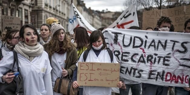 A nursing student holds a banner reading 'ESI (Nursing students - phonetically sounding like 'what if') we demonstrate?, ESI we moved forward?' on March 4, 2014 in Lyon during a nursing students' demonstration against a decision by private clinics to block nursing students from interning. The protest was part of a national movement by nursing students against the decision taken by private clinics not to accept nursing student interns as a reaction against the government's recent effort to lower the fees of their services. AFP PHOTO / JEFF PACHOUD (Photo credit should read JEFF PACHOUD/AFP/Getty Images)