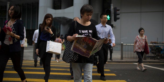 A woman reads a newspaper as she crosses a street in the business district of Central in Hong Kong, China, on Tuesday, Oct. 1