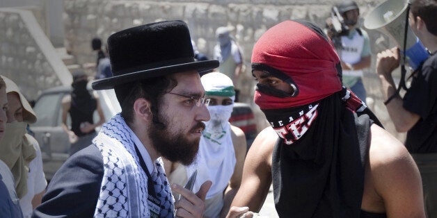 A member of Neturei Karta, a fringe of ultra-Orthodox movement within the anti-Zionist bloc in Israel, talks with a masked Palestinian youth during clashes with Israeli police in the Arab east Jerusalem neighbourhood of Silwan on April 25, 2010. Palestinian protesters clashed with Israeli police as dozens of ultra-nationalist Jews carried Israeli flags through Silwan to assert Jewish sovereignty of all of Jerusalem, according to the organisers of the march. AFP PHOTO/MENAHEM KAHANA (Photo credit should read MENAHEM KAHANA/AFP/Getty Images)