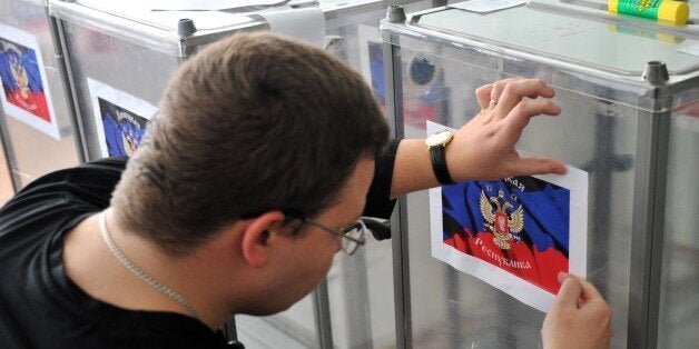 A member of the regional election commission glues a sticker depicting the flag of the self-proclaimed Donetsk People's Republic atop of Ukraine's state emblem, as he prepares ballot boxes, in Donetsk, eastern Ukraine, on May 10, 2014, on the eve of a referendum on independence. Preparations were in full swing on Saturday for the disputed referendums in the two eastern regions of Donetsk and Lugansk, home to 7.3 million of Ukraine's total population of 46 million. Voters in Sunday's referendums will be asked if they support the creation of two independent republics that many see as a prelude to joining Russia, as happened in Crimea. Ukrainian authorities have, however, poured scorn on the planned referendum, saying it is totally illegitimate. AFP PHOTO / GENYA SAVILOV (Photo credit should read GENYA SAVILOV/AFP/Getty Images)