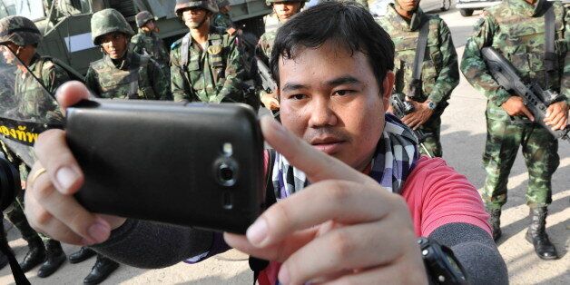 BANGKOK, THAILAND - MAY 22: A member of the press takes a 'selfie' with Thai army soldiers standing guard at the grounds of the venue for peace talks between pro- and anti-government groups on May 22, 2014 in Bangkok, Thailand. The army chief announced in an address to the nation that the armed forces were seizing power amid reports that leaders of the opposing groups attending the talks were being detained by the military. Thailand has seen months of political unrest and violence which has claimed at least 28 lives. (Photo by Rufus Cox/Getty Images)