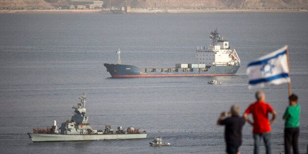 The Panamanian-flagged Klos-C is escorted into the southern Israeli port of Eilat by Israeli warships on March 8, 2014 after it was intercepted by the Israeli navy with the military saying it was carrying advanced rockets from Iran to Gaza. Israeli naval commandos seized the vessel on March 5, 2014 in the Red Sea between Eritrea and Sudan, as it was said to carry on Iranian shipment of M-302 rockets destined for the Hamas-run Gaza Strip. In the foreground people wave an Israeli flag. AFP PHOTO /JACK GUEZ (Photo credit should read JACK GUEZ/AFP/Getty Images)