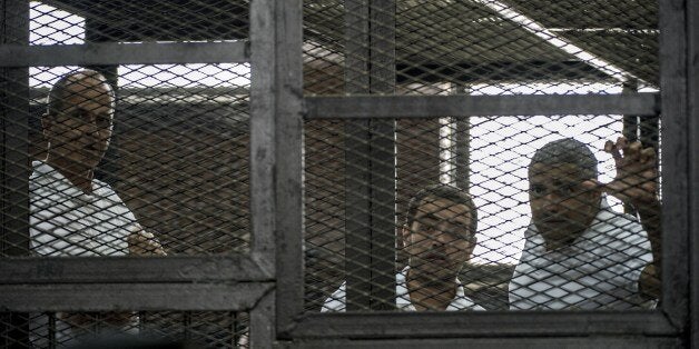 Al-Jazeera news channel's Australian journalist Peter Greste (L) and his colleagues, Egyptian-Canadian Mohamed Fadel Fahmy (R) and Egyptian Baher Mohamed (C), listen to the verdict inside the defendants cage during their trial for allegedly supporting the Muslim Brotherhood on June 23, 2014 at the police institute near Cairo's Tora prison. The Egyptian court sentenced the three Al-Jazeera journalists to jail terms ranging from seven to 10 years after accusing them of aiding the blacklisted Brotherhood. Since the army ousted Islamist president Mohamed Morsi in July 2013, the authorities have been incensed by the Qatari network's coverage of their deadly crackdown on his supporters. AFP PHOTO / KHALED DESOUKI (Photo credit should read KHALED DESOUKI/AFP/Getty Images)