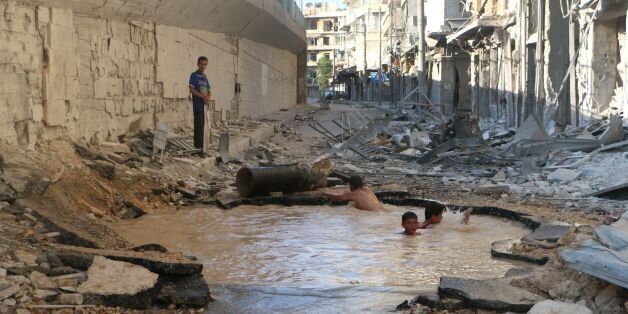 Syrian children play in a bomb crater flooded with water from a broken mains in the northern city of Aleppo, on July 10, 2014. Since the conflict between rebel fighter and pro-Syrian forces erupted in 2011, much of the infrastructure in effected cities has been damaged or destroyed. AFP PHOTO/AMC/FADI AL-HALABI (Photo credit should read Fadi al-Halabi/AFP/Getty Images)
