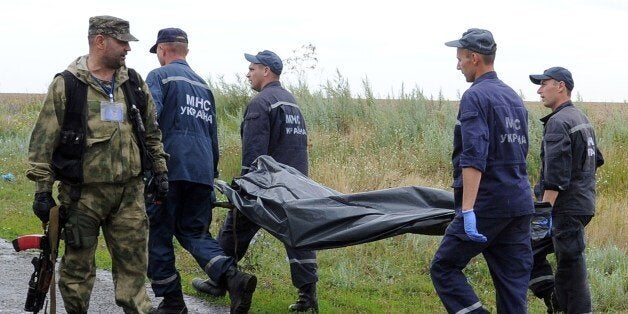 Ukrainian rescue workers walk past an armed pro-Russia militant as they carry the body of a victim on a stretcher at the site
